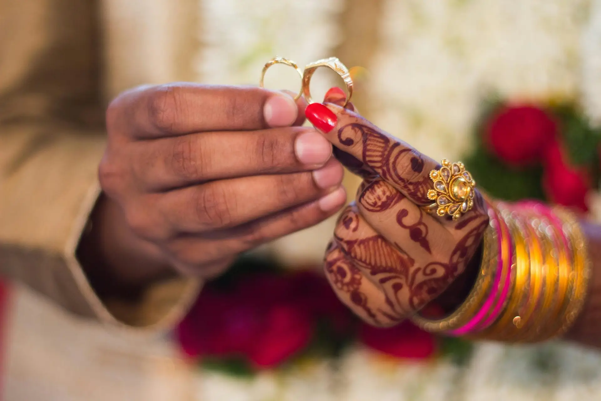Close-up of hands with henna and jewelry during a traditional Indian wedding ceremony, exchanging rings.