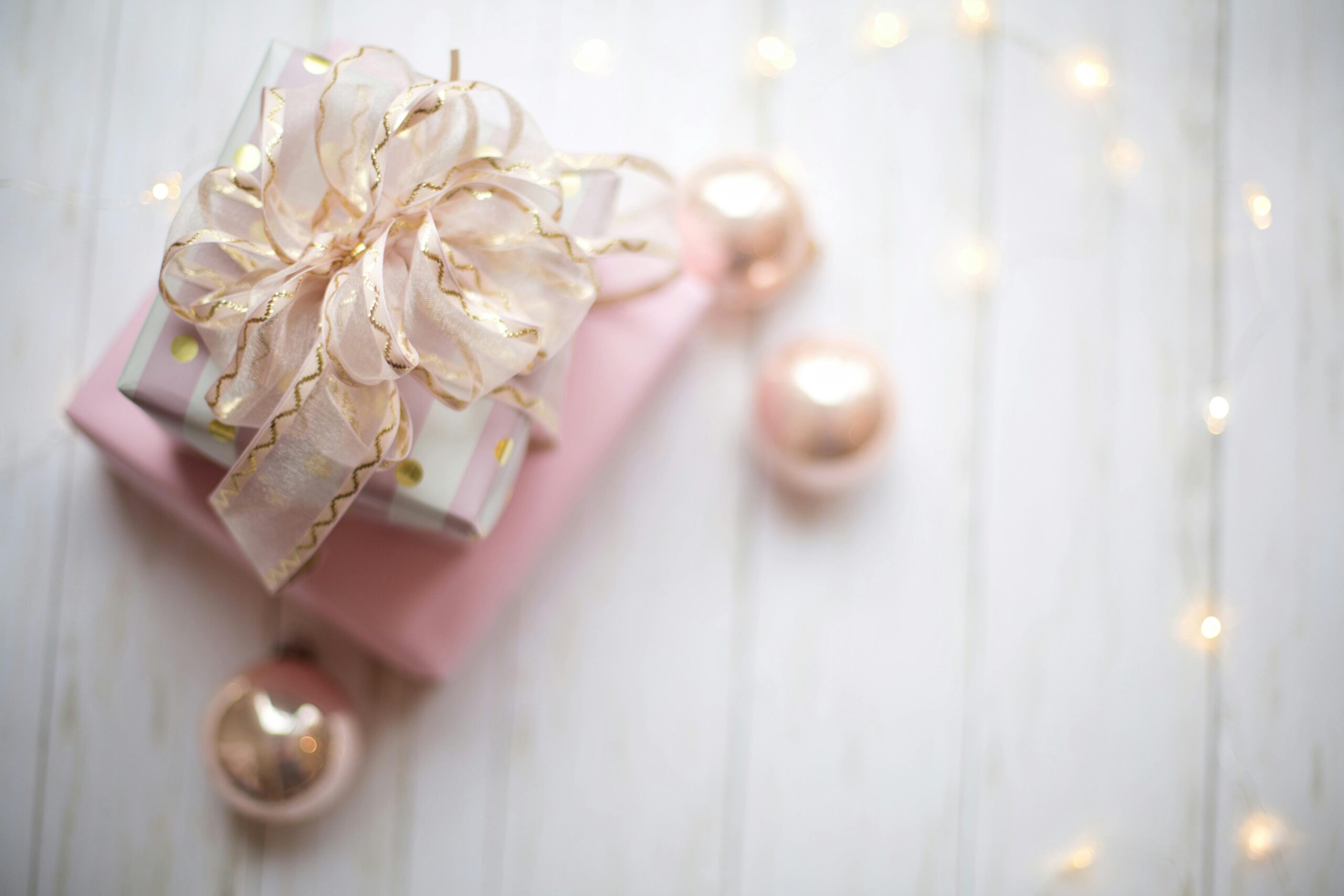 Top view of a beautifully wrapped gift with rose gold ornaments and soft lighting, perfect for celebrations.