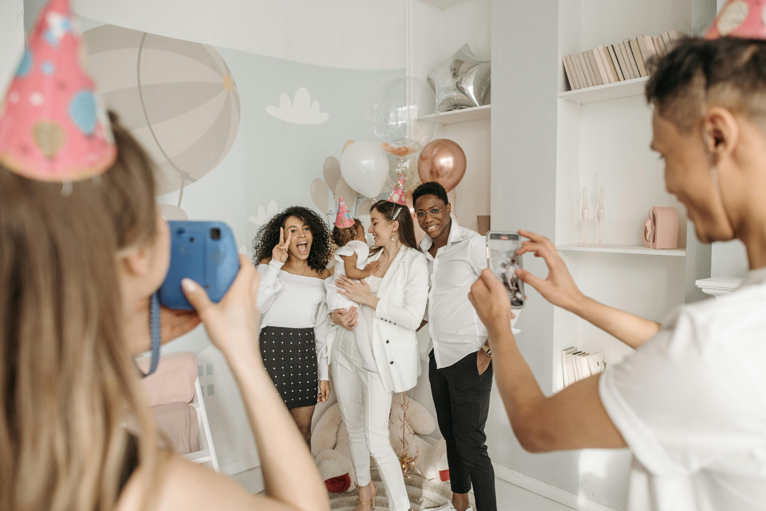 Group of friends celebrating a birthday indoors with balloons and party hats, captured in a joyful moment.